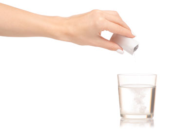 Individual tipping an open sachet into a glass of water